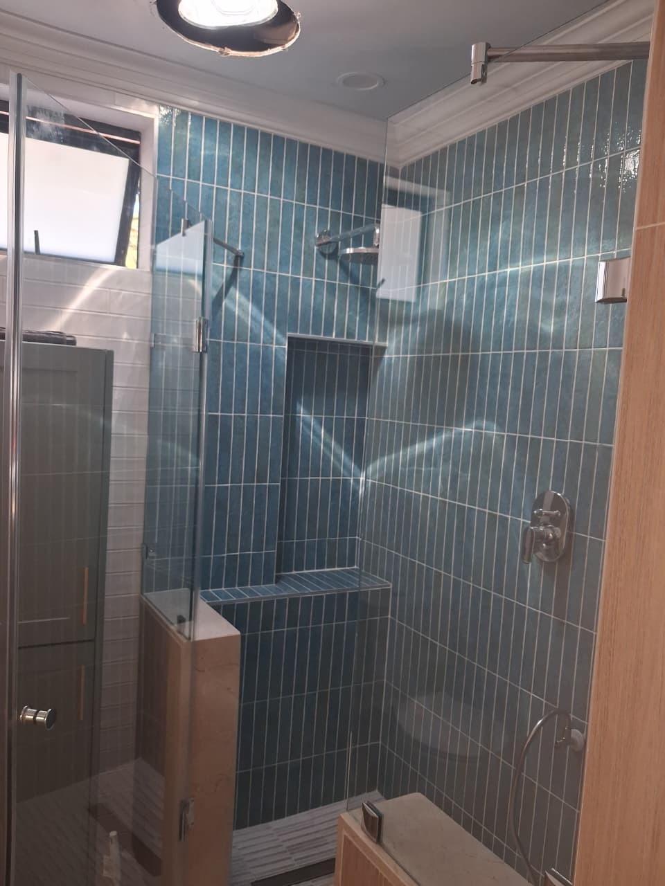 Completed walk-in shower with teal subway tiles and a glass enclosure