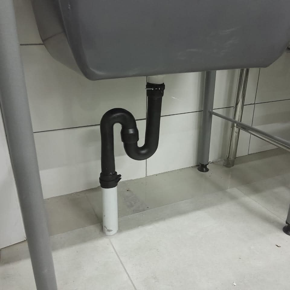 Black S-trap drain assembly connecting a utility sink to PVC floor pipe