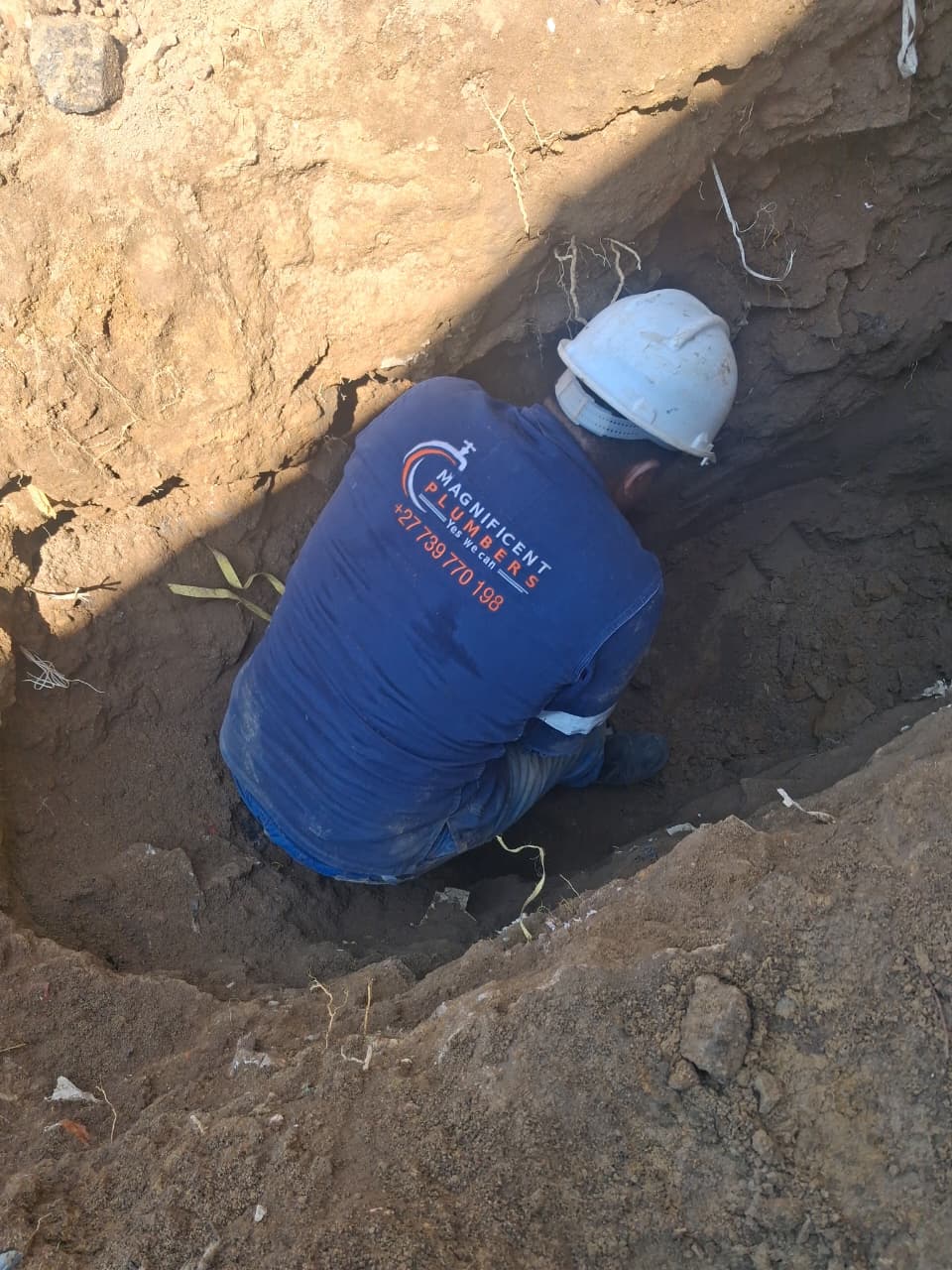 Plumber in a hard hat working inside a deep excavation on site