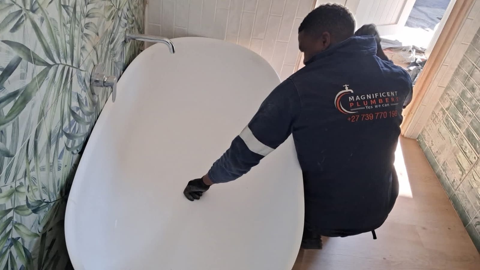 Plumber installing a white freestanding bathtub with leaf-patterned tiles